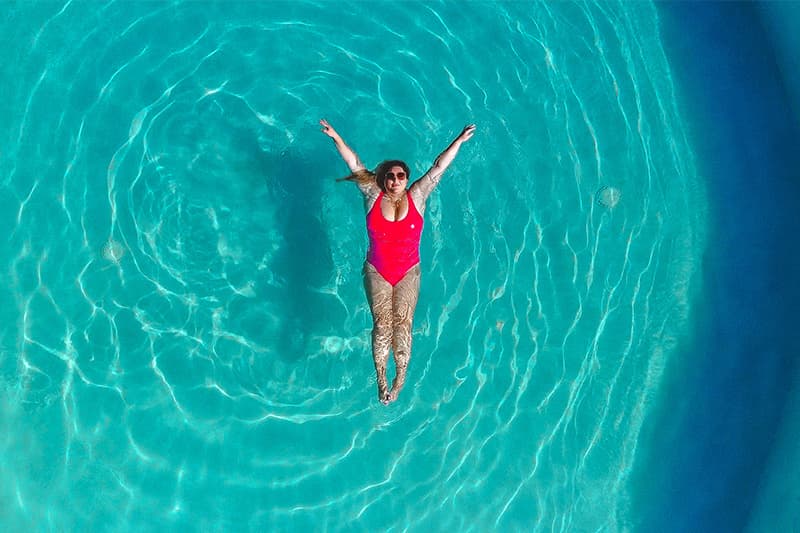 A woman in a red swimsuit floats on her back in a turquoise swimming pool. A woman in a red swimsuit floats on her back in a turquoise swimming pool.