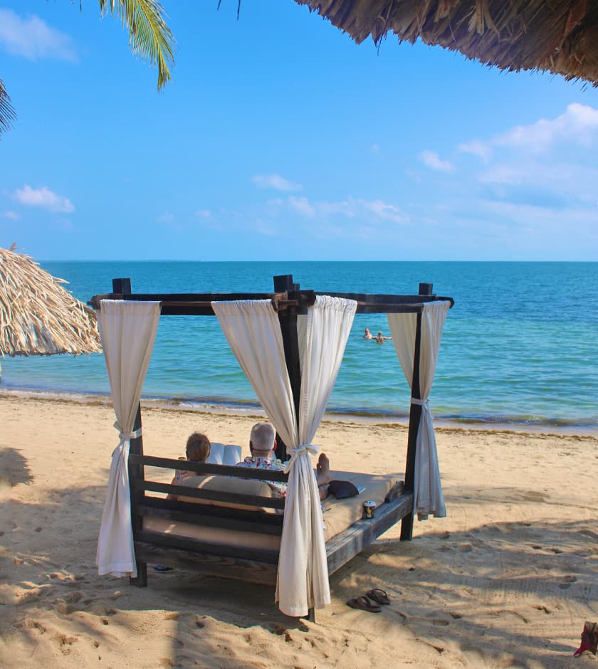 A couple relaxes on a beach cabana overlooking the calm sea.