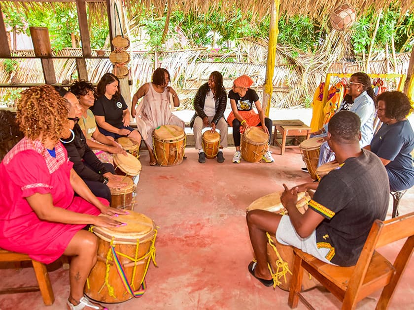 A diverse group of people gather in a rustic setting to play hand drums in a circle. A diverse group of people gather in a rustic setting to play hand drums in a circle.