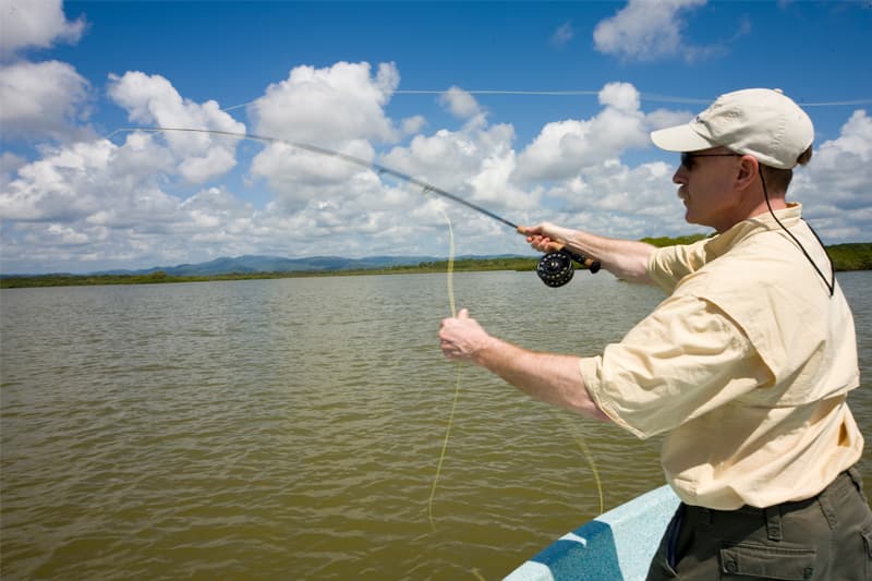 A man fly-fishing on a lake under a partly cloudy sky.