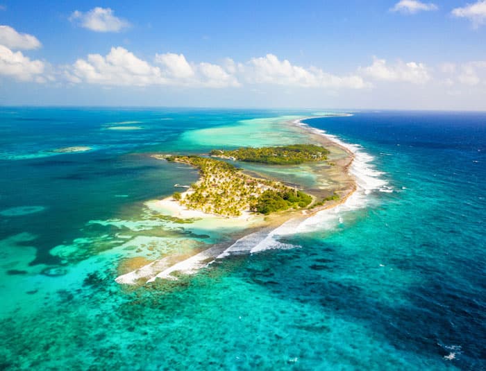 A breathtaking aerial view of Manta Island Resort, showcasing the pristine white sand beaches, lush vegetation, and crystal-clear turquoise waters of Glover's Reef, Belize.