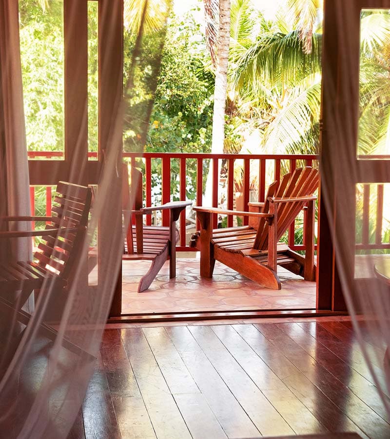 A cozy wooden porch with two chairs surrounded by lush greenery.