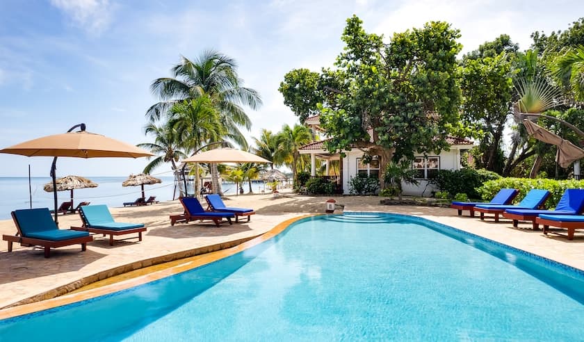 A serene poolside view featuring lounge chairs, umbrellas, and tropical foliage near the ocean.