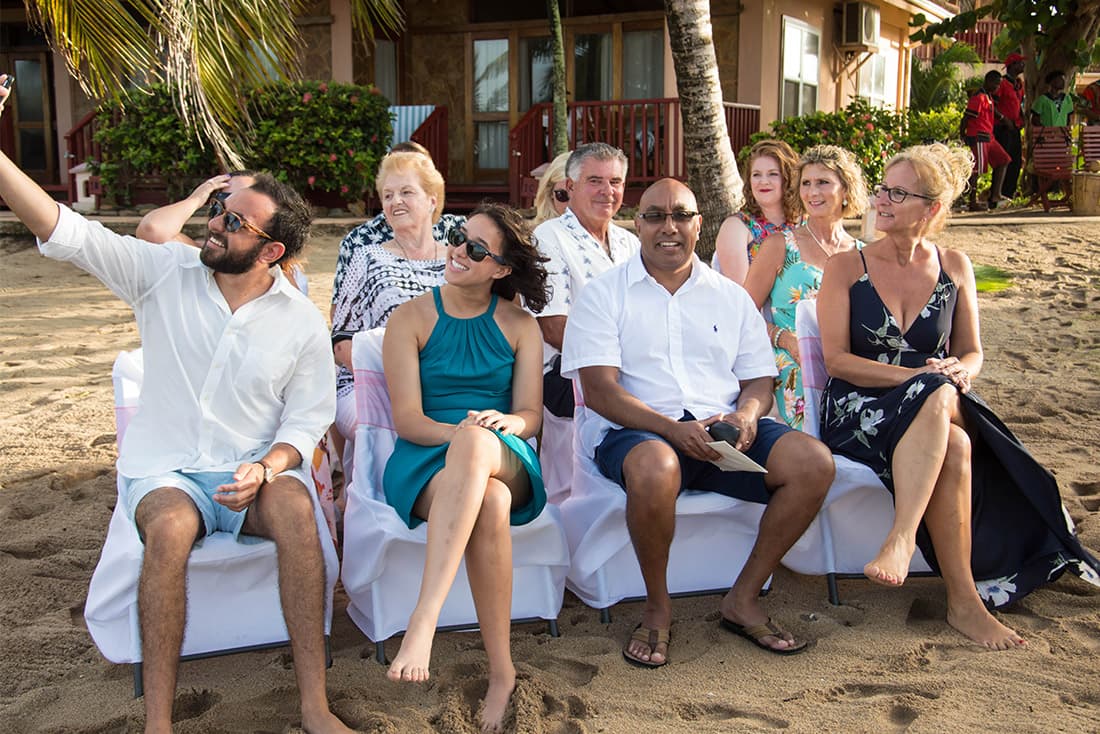 Wedding attendees sitting on chairs in sand covered in white cloth.