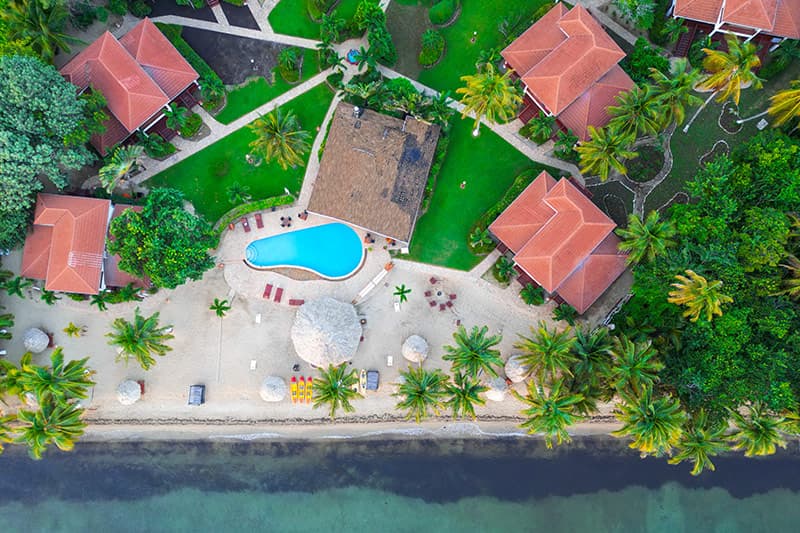 Aerial view of a beach resort with a swimming pool, palm trees, and cabanas. Aerial view of a beach resort with a swimming pool, palm trees, and cabanas.