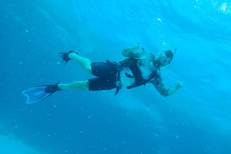 A diver gives a thumbs-up underwater amidst swirling bubbles.