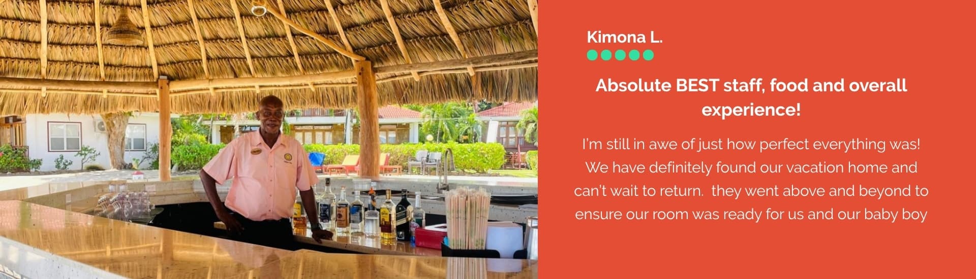 A smiling staff member stands behind a bar in a tropical setting, showcasing bottles and drinks.