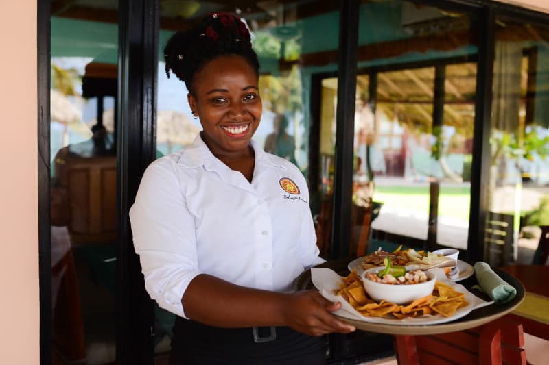 A waitress smiles while holding a tray of food in a restaurant setting.