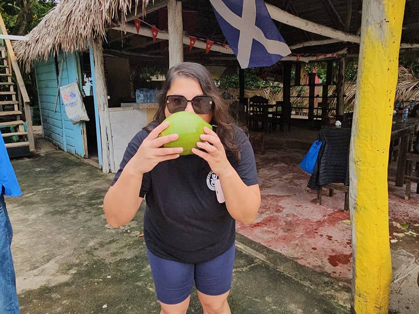 Person wearing sunglasses holds a green coconut while standing in an outdoor setting. Person wearing sunglasses holds a green coconut while standing in an outdoor setting.