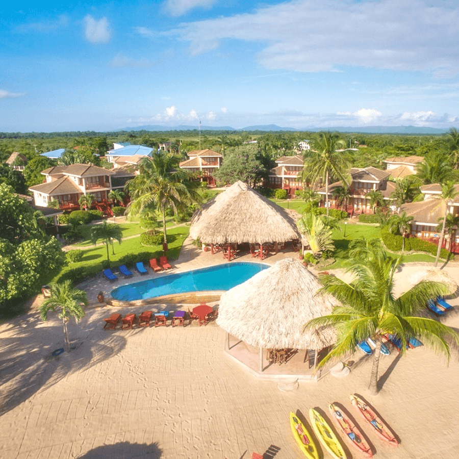 An aerial view of a tropical resort with a pool, beach, and thatched-roof structures.