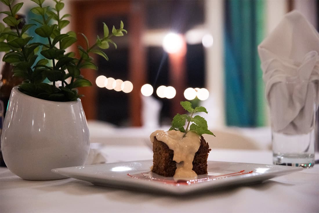 Desert cake and topping on a white plate, with white linens, glass with napkin and potted plant.