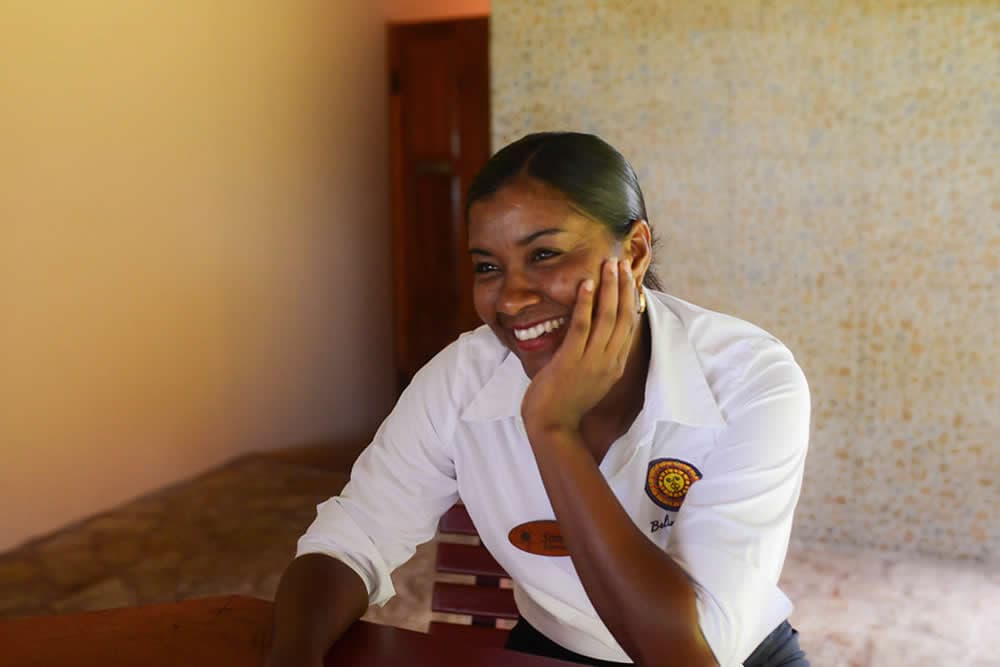 Smiling woman at front desk in white shirt with Belizean Dreams Resort logo.