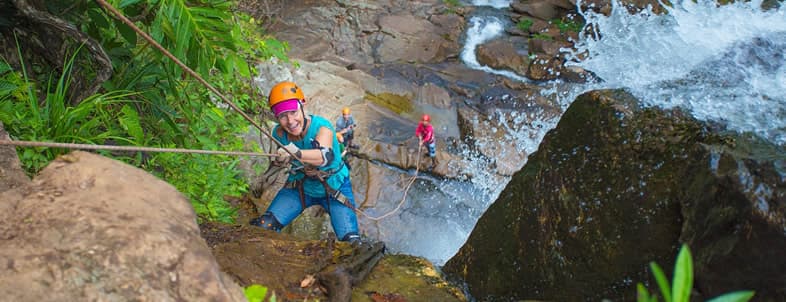 Two climbers ascend a waterfall, with one person using a rope and harness on rocky terrain. Two climbers ascend a waterfall, with one person using a rope and harness on rocky terrain.