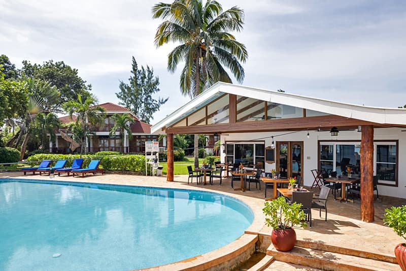 A beachfront villa with a pool surrounded by lush greenery and seating areas.