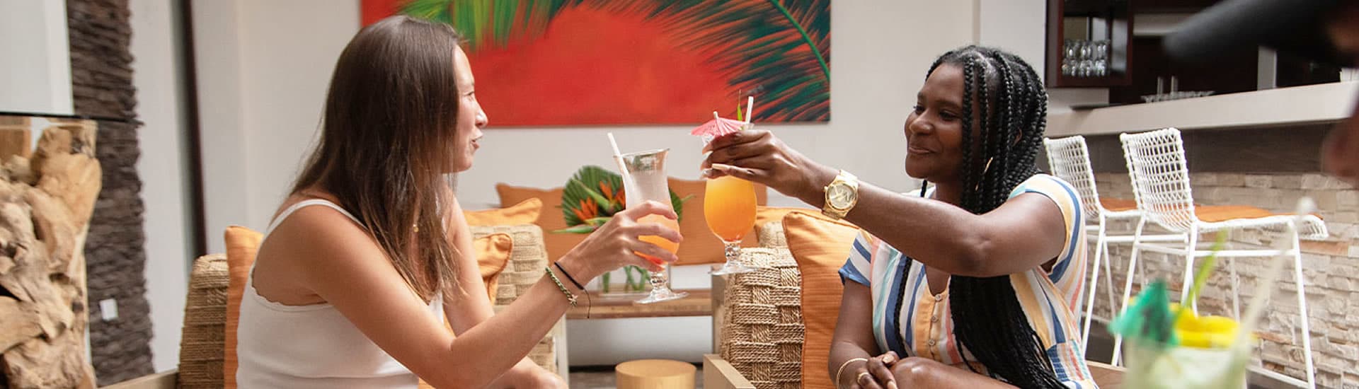 Two women in a lounge area toast each other with tequila sunrise cocktails.