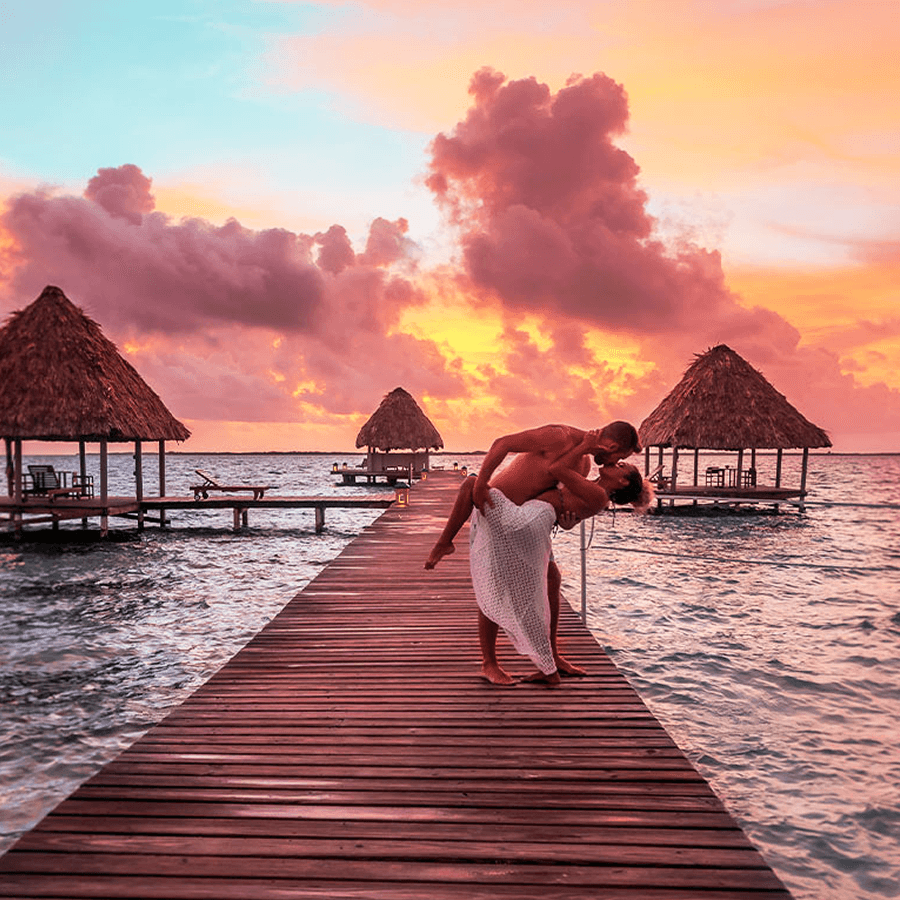 Romantic photo of a man dipping a woman on a pier overlooking the ocean against a beautiful sunset.