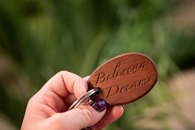 A person holds a wooden keychain engraved with "Belizean Dreams."