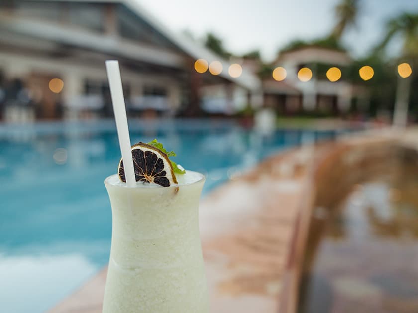 A refreshing cocktail with a slice of dried lime sits beside a swimming pool. A refreshing cocktail with a slice of dried lime sits beside a swimming pool.