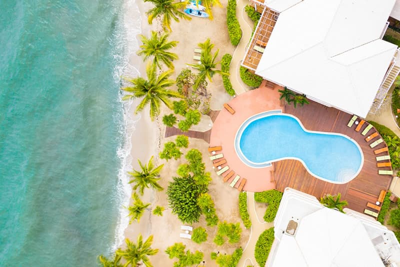 Aerial view of a pool next to a sandy beach and palm trees.