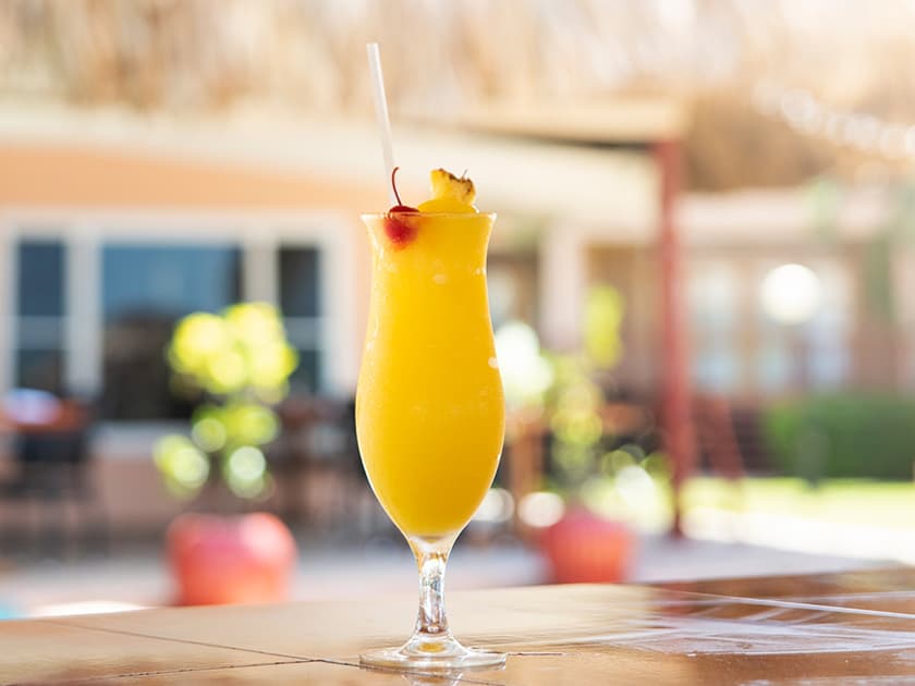 A bright yellow cocktail with a cherry and pineapple garnish in a tall glass.