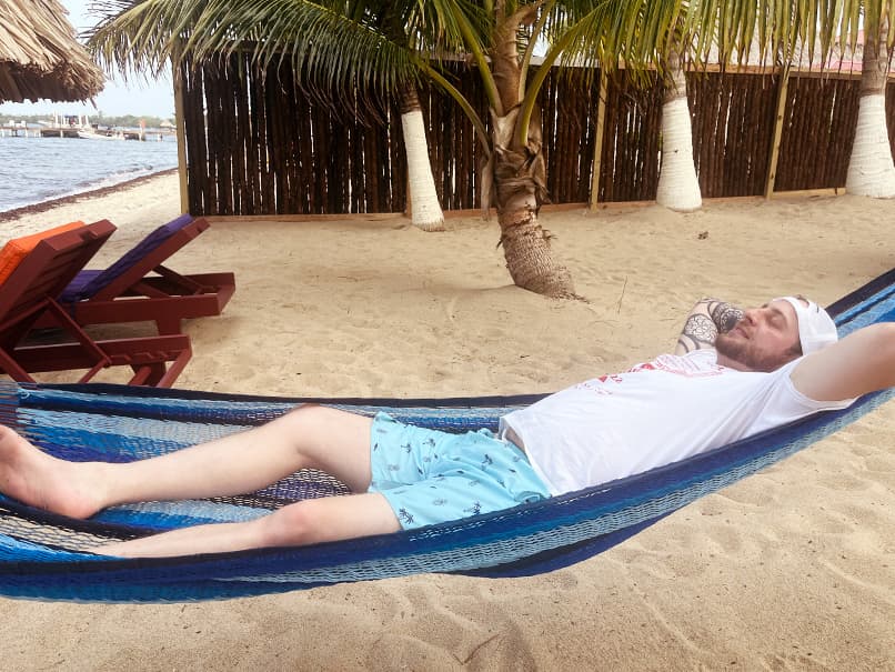 A man relaxes in a hammock on the beach under palm trees. A man relaxes in a hammock on the beach under palm trees.