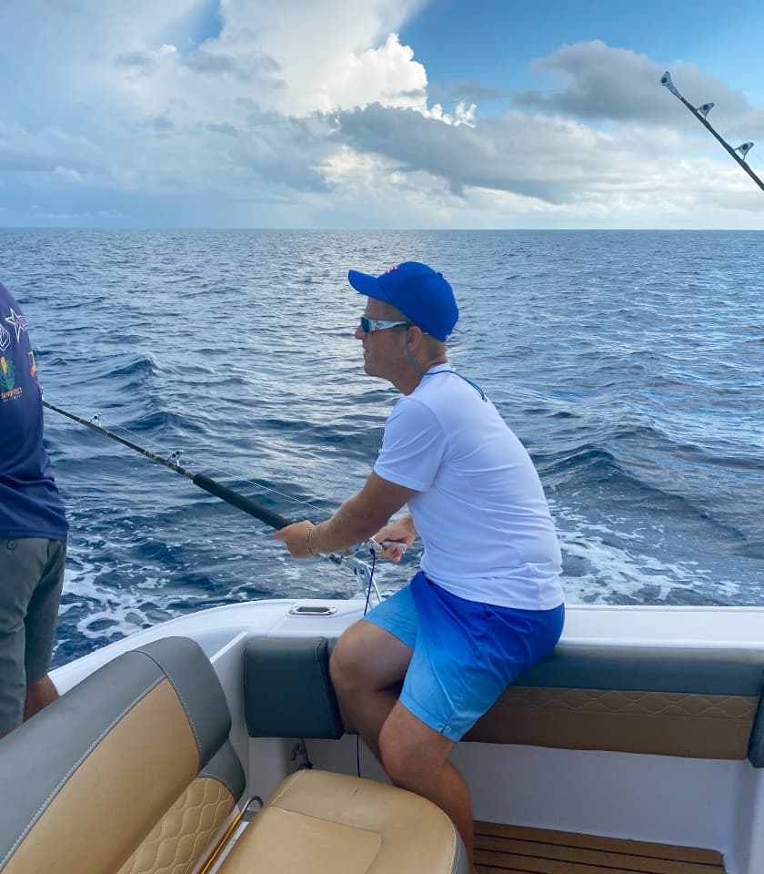 A man fishing from a boat in the ocean under a cloudy sky.