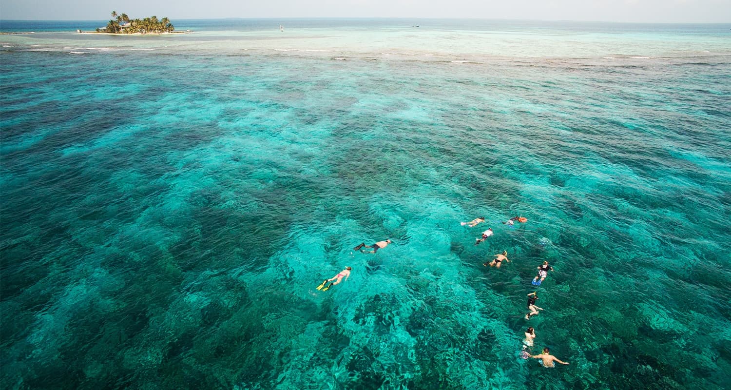 Large Group of snorkelers in ocean with island in background.