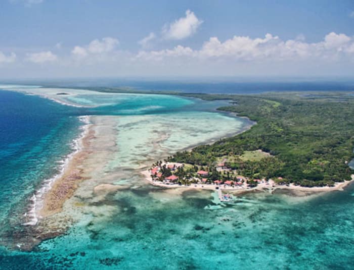Aerial view of a tropical island in Belize, featuring white sand beaches, turquoise waters, and a vibrant coral reef.