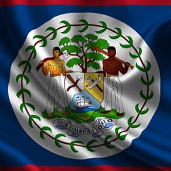The flag of Belize, featuring a blue field with a white circle in the center containing the national coat of arms. The coat of arms depicts two men standing on either side of a mahogany tree, holding a paddle and an axe. The motto "Sub umbra floreo" is written below the tree.