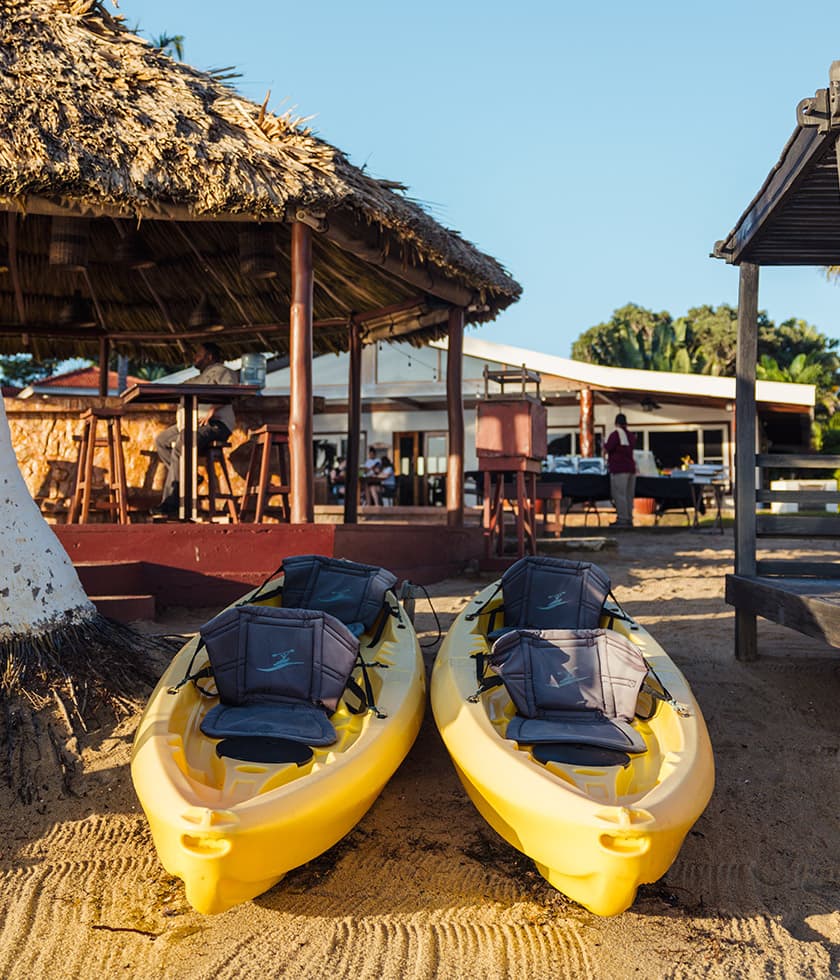 Two yellow kayaks sit on the sandy beach near a thatched-roof hut.