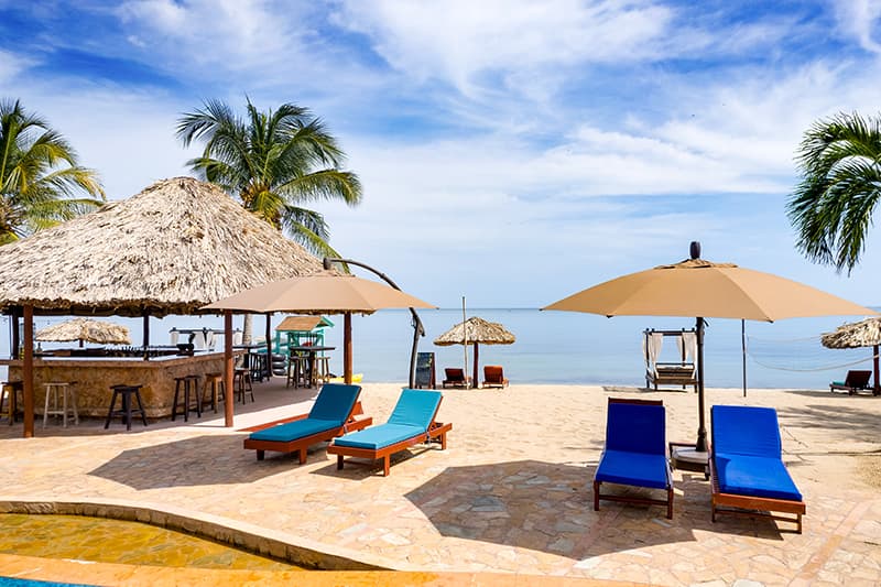 Tropical beach scene with lounge chairs, umbrellas, and thatched-roof huts by the sea. Tropical beach scene with lounge chairs, umbrellas, and thatched-roof huts by the sea.