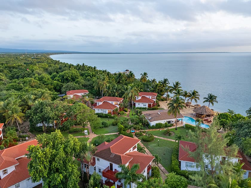 Aerial view of a coastal resort with red-roofed buildings surrounded by lush greenery and a serene ocean. Aerial view of a coastal resort with red-roofed buildings surrounded by lush greenery and a serene ocean.