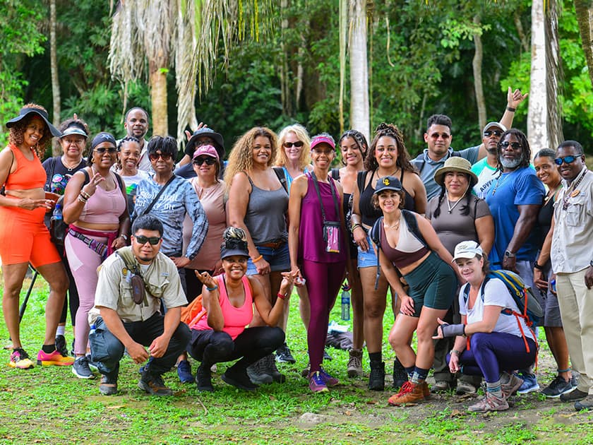 A diverse group of hikers poses together in a lush, green outdoor setting.