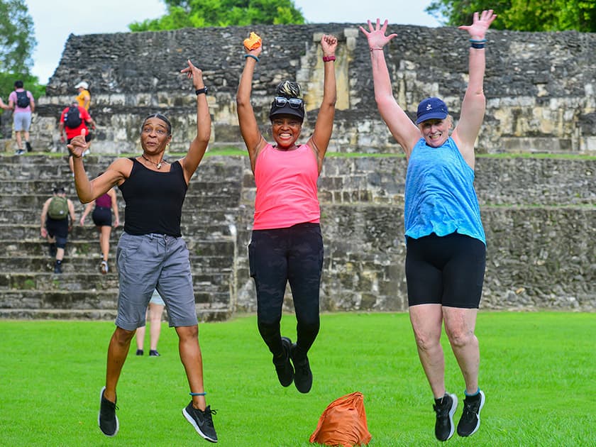 Three women joyfully jumping in front of ancient ruins.