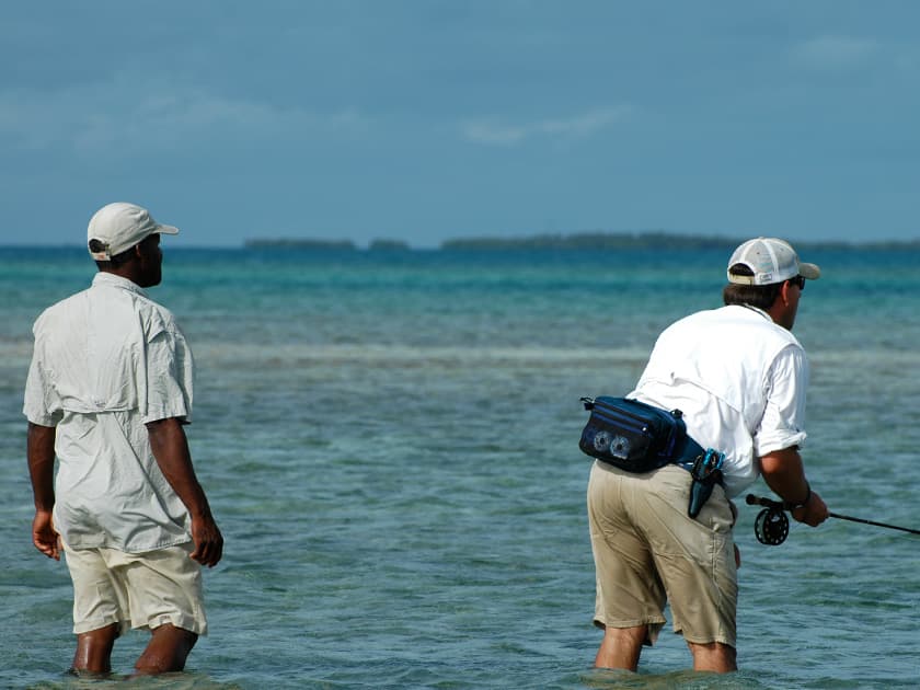Two men wade through shallow water while fishing in a tropical setting. Two men wade through shallow water while fishing in a tropical setting.