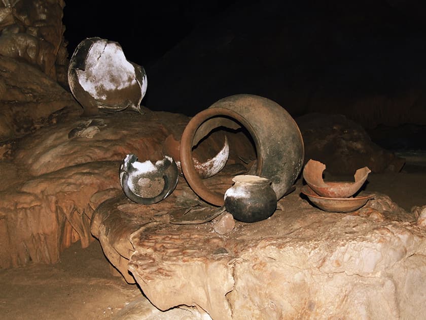 Ancient pottery fragments are scattered on a rocky cave floor.