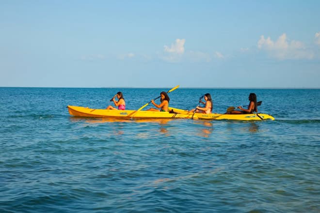 Four people kayaking in a bright yellow kayak on calm blue waters.