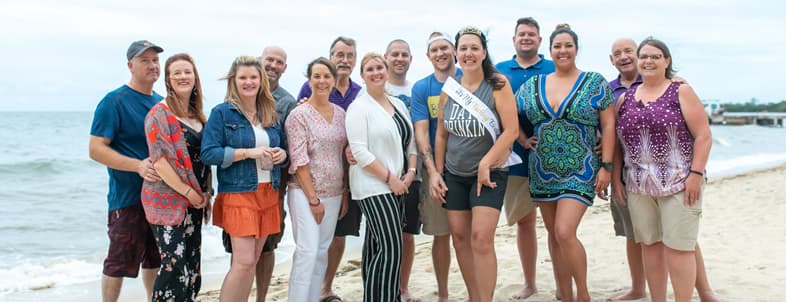 A group of people stands together on a beach, smiling and posing for a photo. A group of people stands together on a beach, smiling and posing for a photo.