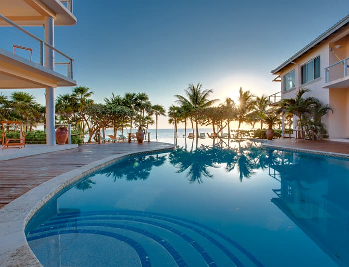 A serene poolside view at sunset, surrounded by palm trees and a coastal backdrop.
