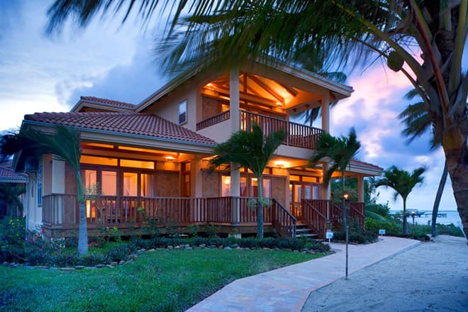 A coastal villa illuminated at dusk, surrounded by palm trees and a landscaped lawn.