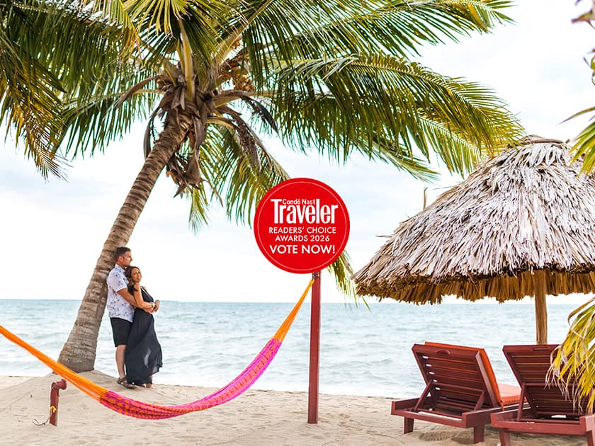 A couple embraces on a beach with palm trees and a straw hut, featuring a promotional sign for the Condé Nast Traveler Readers' Choice Awards 2026. A couple embraces on a beach with palm trees and a straw hut, featuring a promotional sign for the Condé Nast Traveler Readers' Choice Awards 2026.