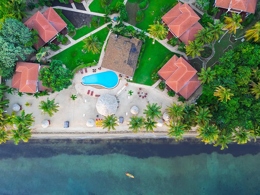 Aerial view of a tropical resort featuring a pool, palm trees, and beachside bungalows. Aerial view of a tropical resort featuring a pool, palm trees, and beachside bungalows.