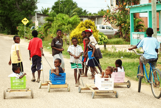 Children play with makeshift wagons on a street in a vibrant neighborhood.
