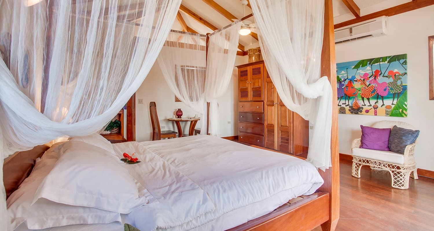 Lodging Accommodation room, with 4 poster light color wood bed, with bright artwork on wall, and hardwood floors.