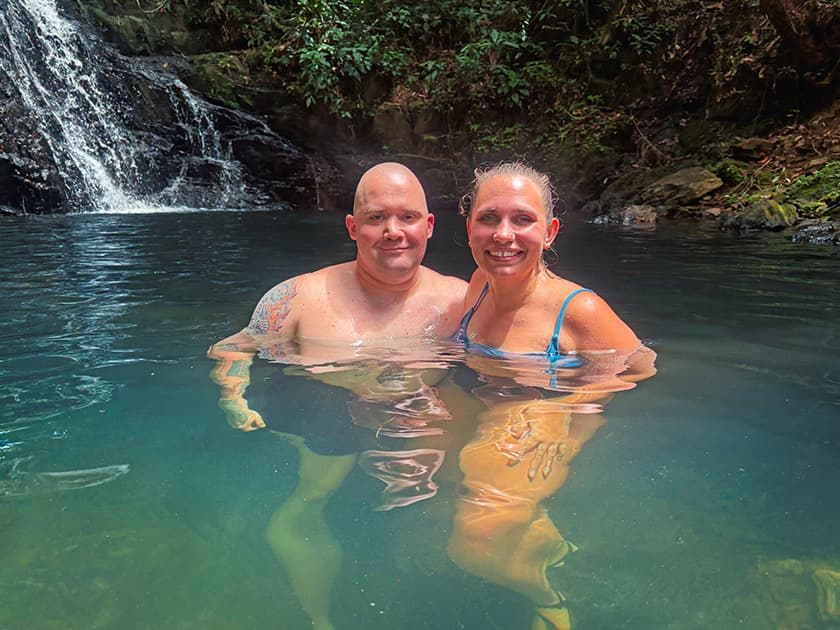 A man and a woman are smiling while wading in a natural pool near a waterfall. A man and a woman are smiling while wading in a natural pool near a waterfall.