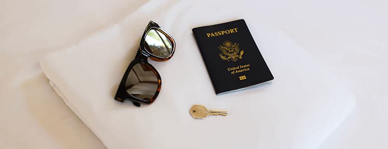 Sunglasses, a key, and a U.S. passport are arranged on a white surface.