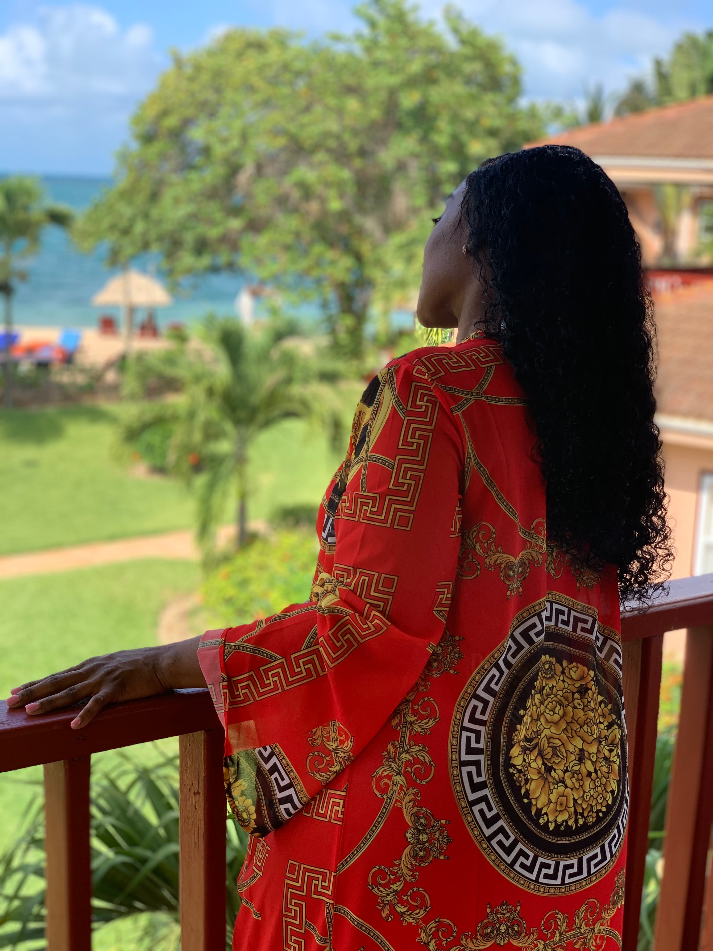 Woman with dark hair and tropical red dress looking out at the ocean from her balcony.