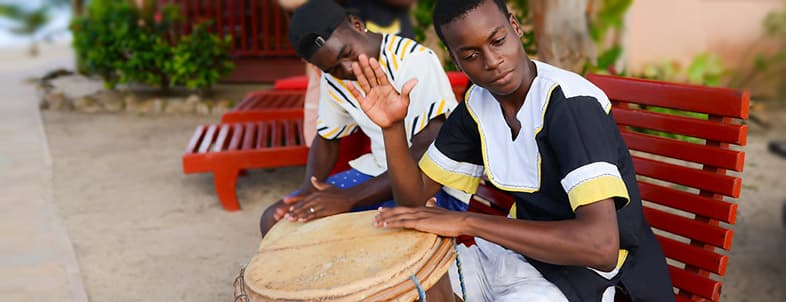 Two boys in traditional clothing play drums on a beachside. Two boys in traditional clothing play drums on a beachside.