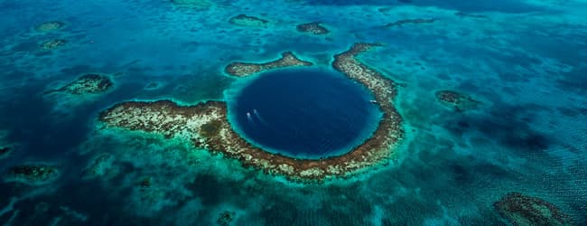 Aerial view of the Great Blue Hole surrounded by turquoise waters and coral reefs. Aerial view of the Great Blue Hole surrounded by turquoise waters and coral reefs.