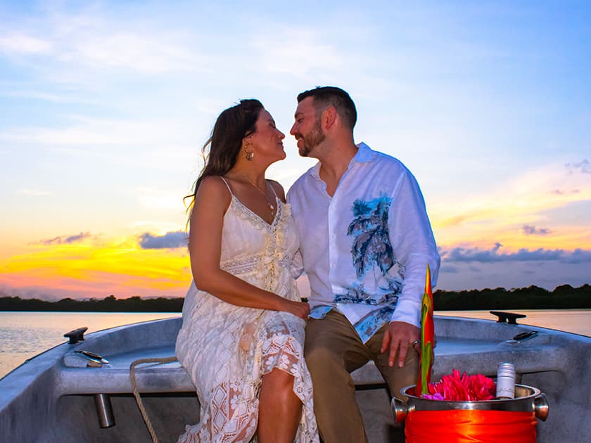 A couple embraces on a boat at sunset, surrounded by nature.